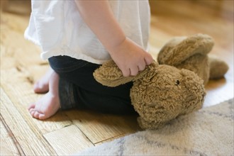 Baby girl (18-23 months) kneeling on floor and holding teddy bear