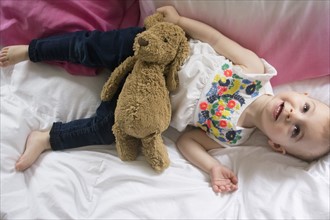 Girl (18-23 months) lying on bed with teddy bear