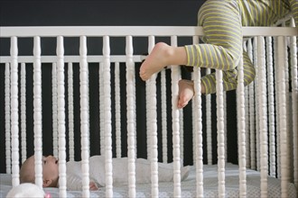 Girl (2-3) climbing on crib and brother (6-11 months) lying inside