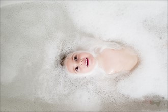 Girl (2-3) lying in bathtub
