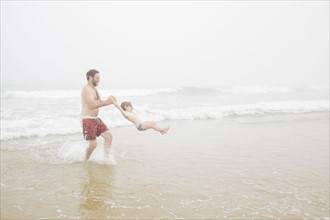 USA, New York, Monatuk, Father spinning daughter (2-3) on beach by ocean