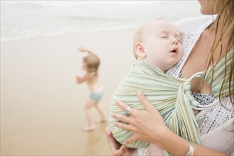 Mother holding baby son (6-11 months), daughter (2-3) dancing on beach