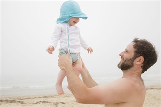 Father lifting baby son (6-11 months) on beach