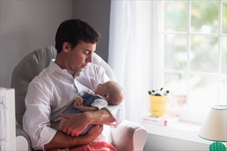 Father holding baby son (0-1 months) by window