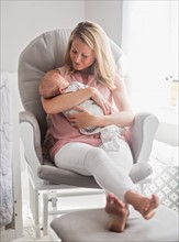 Mother sitting in armchair and holding baby son (0-1 months)