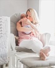 Mother sitting in armchair and holding baby son (0-1 months)