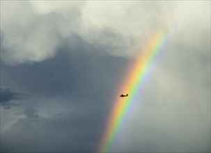 Silhouette of small plane flying through rainbow