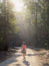 Australia, New South Wales, Port Macquarie, Rear view of mature woman walking along dirt road in forest