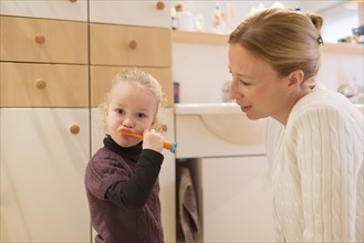 Mother looking at daughter (4-5) brushing teeth in bathroom