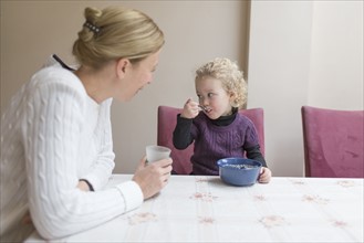 Mother looking at daughter (4-5) eating breakfast