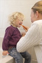 Mother brushing daughter's teeth (4-5) in bathroom
