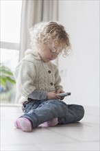 Blond girl (4-5) sitting on floor and playing with mobile phone