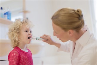 Mother helping daughter (4-5) brush teeth