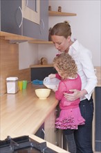 Mother helping daughter (4-5) pour milk into bowl