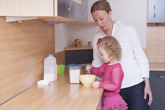 Mother watching daughter (4-5) mixing ingredients in bowl