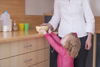 Mother helping daughter (4-5) take bowl from kitchen counter