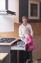 Mother helping daughter (4-5) sort kitchen utensils in drawer