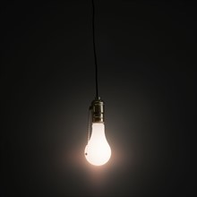 Light bulb hanging against grey background.