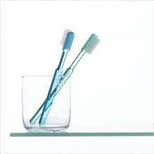 Toothbrushes in glass on shelf.