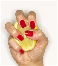 Hand of woman with red nail polish squeezing lemon.