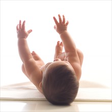 Naked baby girl (6-11 months) lying on back and reaching up.