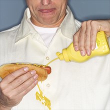 Mature man holding hotdog and accidentally spilling mustard on shirt.