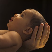 Profile view of baby girl (6-11 months) with head supported by hand of man.