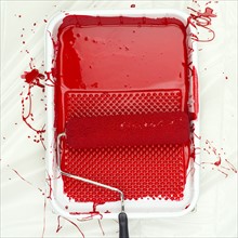 Paint roller on tray with red paint.