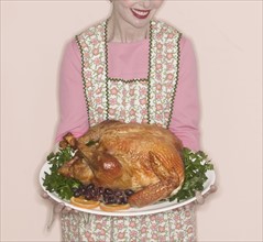 Smiling senior woman holding garnished turkey on plate.