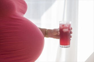 Mid section of pregnant woman in red blouse holding red drink