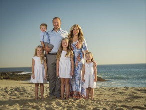 Family with children (12-17 months, 4-5, 6-7, 8-9) standing on beach with sea in background
