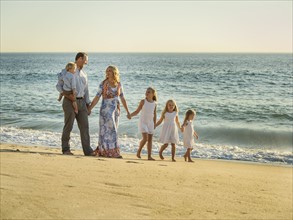 Family with children (12-17 months, 4-5, 6-7, 8-9) walking on beach with sea in background