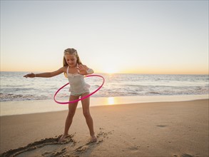 Girl (8-9) spinning plastic hoop on beach