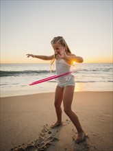 Girl (8-9) spinning plastic hoop on beach