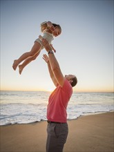 Father throwing daughter (4-5) in air on beach