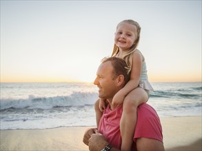 Father carrying daughter (4-5) on beach