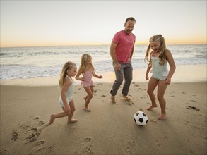 Father with children (4-5, 6-7, 8-9) playing soccer on beach