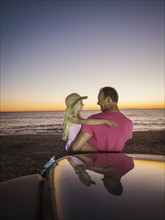 Father carrying daughter (4-5) next to car on beach