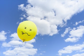 Yellow balloon with drawn face against blue sky