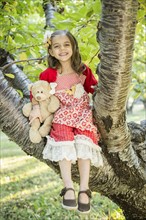 Girl with teddy bear sitting on tree