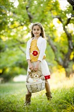 Smiling girl standing in orchard, holding basket with teddy bear