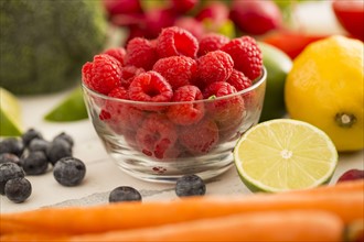 Raspberries in bowl surrounded by fruits and vegetables