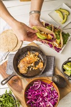 Woman preparing tortilla with tilapia, avocado and red cabbage