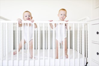 Twin brothers (12-17 months) standing in crib