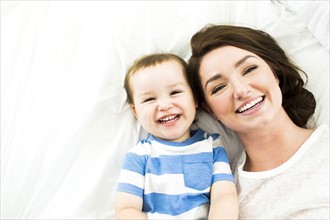 Mother lying with son (4-5) on bed and smiling
