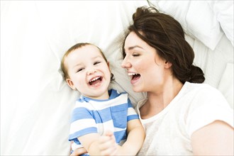 Mother lying with son (4-5) on bed and laughing