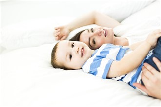 Mother lying with son (4-5) on bed and smiling