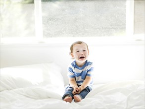 Boy (4-5) sitting on bed and crying
