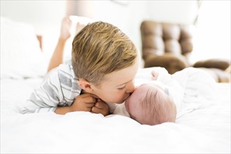Brother (4-5) lying on bed and kissing sister (0-1 months)