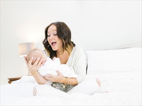 Mother sitting on bed carrying daughter (0-1 months) and laughing